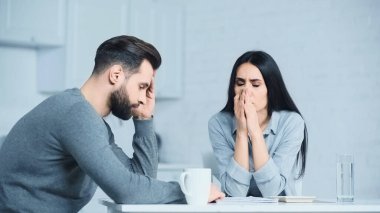 Üzgün, gözleri kapalı, elleri dua eden bir kadın. Evdeki üzgün adam.
