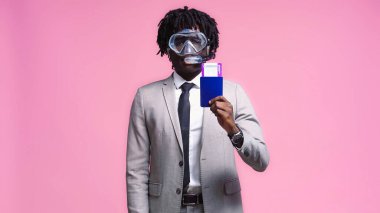 Pasaportu pembe olan, dalgıç maskeli Afrikalı Amerikalı bir işadamı.