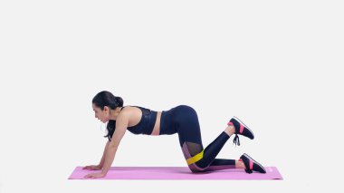 Esmer genç sporcunun yan görünüşü. Beyaz üzerine pembe fitness minderi üzerinde elastiklerle çalışıyor.