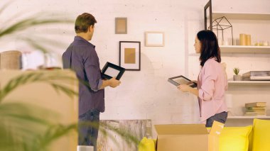 Yeni evde duvarın yanında fotoğraf çerçevesi tutan çift