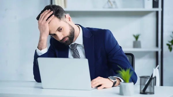 Takım elbiseli üzgün işadamı masadaki laptopa bakıyor.