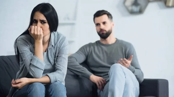 Worried Woman Covering Face Sitting Blurred Displeased Boyfriend Quarrelling Living — 스톡 사진