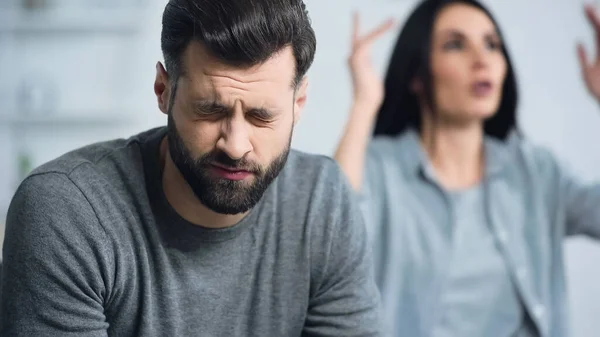 Sad Bearded Man Closed Eyes Listening Blurred Girlfriend Quarrelling Home — 图库照片