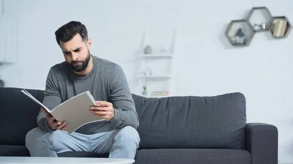 Unzufriedener Mann Schaut Ordner Während Auf Sofa Wohnzimmer Sitzt — Stockfoto