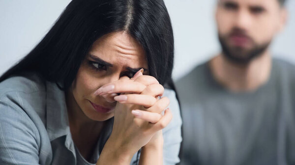 sad woman with clenched hands covering face while crying near blurred man 