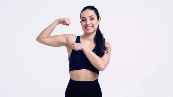 smiling sportswoman pointing at muscle isolated on white