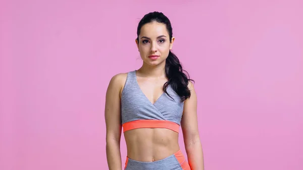 pretty sportswoman in crop top looking at camera isolated on pink