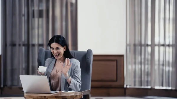 Щаслива Жінка Тримає Чашку Махає Рукою Під Час Відеодзвінка Ноутбуці — стокове фото