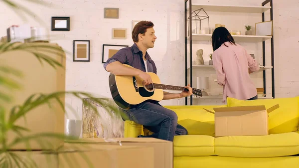 Hombre Tocando Guitarra Acústica Cantando Mientras Mujer Desempacando Nuevo Hogar — Foto de Stock