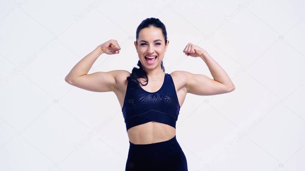 cheerful sportswoman showing muscles isolated on white