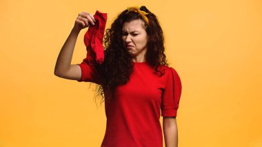 disgusted woman holding smelly socks isolated on orange clipart