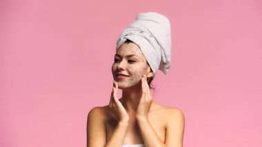 Kafasına havlu geçirmiş neşeli bir kadın pembe bir maske takıyor.