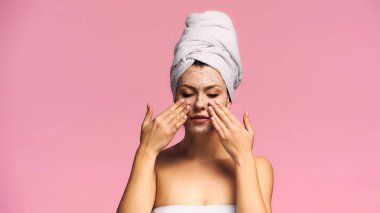 Kafasında beyaz havlu olan genç bir kadın pembe bir maske takıyor.