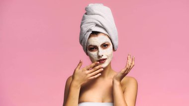 Genç bir kadın kameraya bakarken pembeye izole kilden maske takıyor.