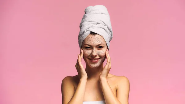 cheerful woman applying cleansing mask and looking at camera isolated on pink