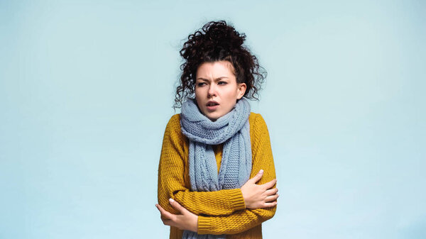 frozen woman in sweater and scarf looking away isolated on blue