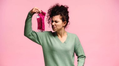 woman feeling disgusted while holding smelly socks isolated on pink clipart