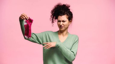 displeased woman pointing at stinky socks and grimacing isolated on pink clipart