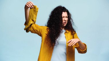 brunette woman feeling disgusted while holding stinky socks isolated on blue clipart