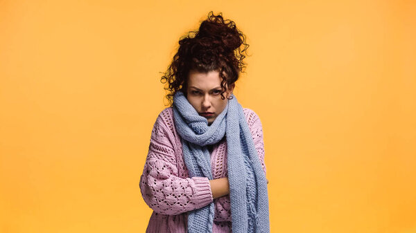 displeased woman freezing in warm sweater and scarf isolated on orange