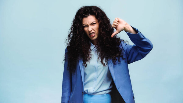 displeased woman grimacing and showing dislike sign isolated on blue