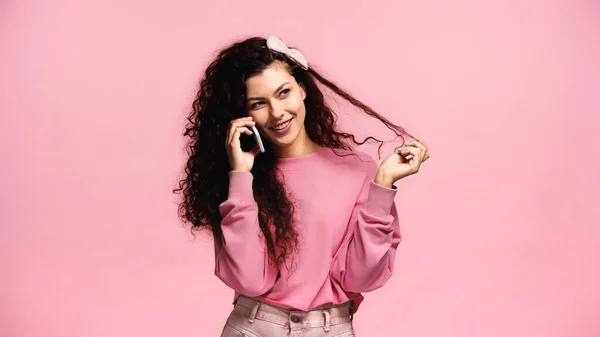 Mujer Complacida Tocando Pelo Mientras Habla Teléfono Celular Aislado Rosa — Foto de Stock