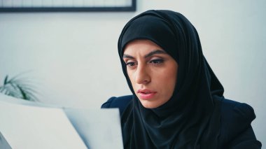 Başörtülü Müslüman iş kadını ofiste bulanık belgelerle çalışıyor 