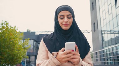 Başörtülü genç Müslüman kadın dışarıda akıllı telefondan mesaj atıyor.