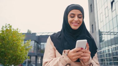 tesettürlü genç müslüman kadın dışarıda cep telefonuyla mesajlaşıyor.