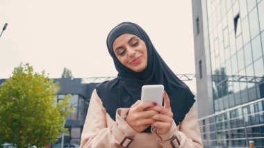 tesettürlü müslüman kadın dışarıda akıllı telefondan mesaj atıyor.