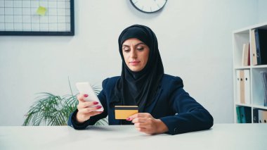 İnternet üzerinden alışveriş yaparken akıllı telefon ve kredi kartı kullanan Müslüman iş kadını 
