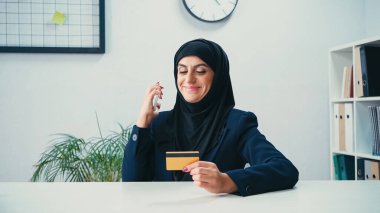 Akıllı telefon ve kredi kartı kullanan neşeli Müslüman iş kadını 