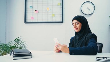 Ofiste akıllı telefon kullanan Müslüman iş kadını 