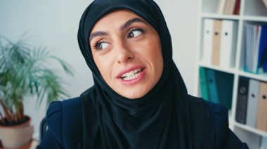 young muslim businesswoman in hijab talking while looking away clipart