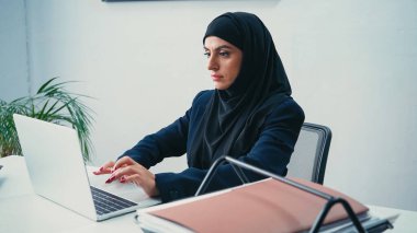 Modern ofiste dizüstü bilgisayarda yazı yazan tesettürlü genç Müslüman iş kadını. 