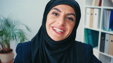 young muslim businesswoman in hijab smiling while looking at camera clipart