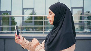 tesettürlü müslüman kadının yan görüntüsü dışarıda akıllı telefondan video çağrısı alıyor. 