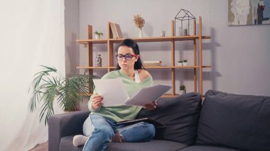 Gözlüklü esmer öğrenci evdeki kağıt klasörün yakınındaki belgelere bakıyor. 