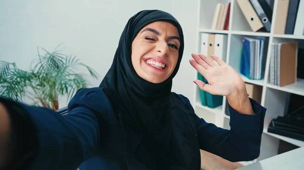 Smiling Muslim Businesswoman Waving Hand While Taking Selfie — Stock Photo, Image