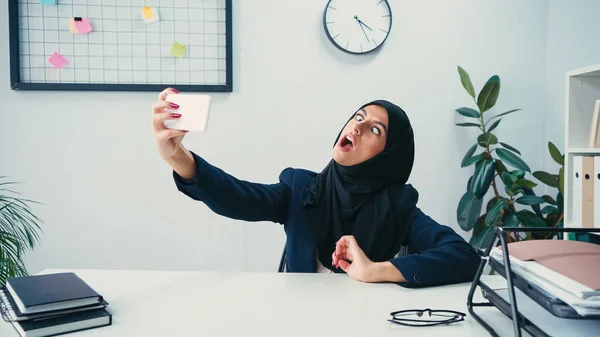 stock image Muslim businesswoman grimacing while taking selfie on smartphone in office 