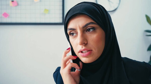 muslim businesswoman in hijab talking on cellphone in office