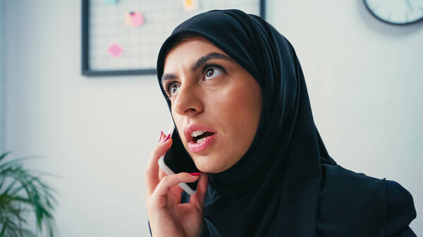 muslim businesswoman in hijab talking on mobile phone in office