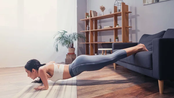 女运动员在沙发和健身垫旁边做俯卧撑的侧视图 — 图库照片