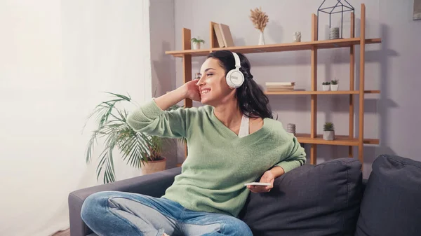 Fröhliche Frau Mit Kopfhörer Hält Smartphone Auf Couch — Stockfoto