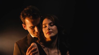 Mutlu adam arkada duruyor ve siyah gözleri kapalı genç bir kadına sarılıyor. 