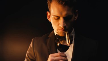 Takım elbiseli kendine güvenen genç adam cam tutuyor ve siyah şarap kokusu alıyor. 