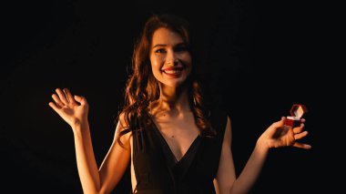 Kırmızı kutulu, alyanslı ve siyah üzerine izole edilmiş hareketler yapan mutlu, genç bir kadın. 