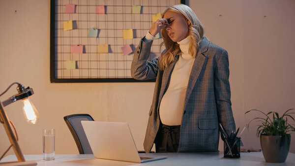 Беременная деловая женщина, страдающая от головной боли в офисе ночью 