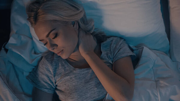 Вид сверху на женщину, страдающую от боли в шее во время сна дома 