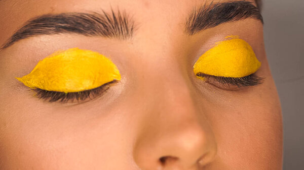partial view of woman applying yellow creamy eye shadow with cosmetic brush